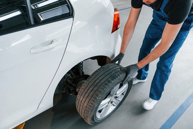 Close up view of man in work uniform with car wheel indoors. Conception of automobile service.
